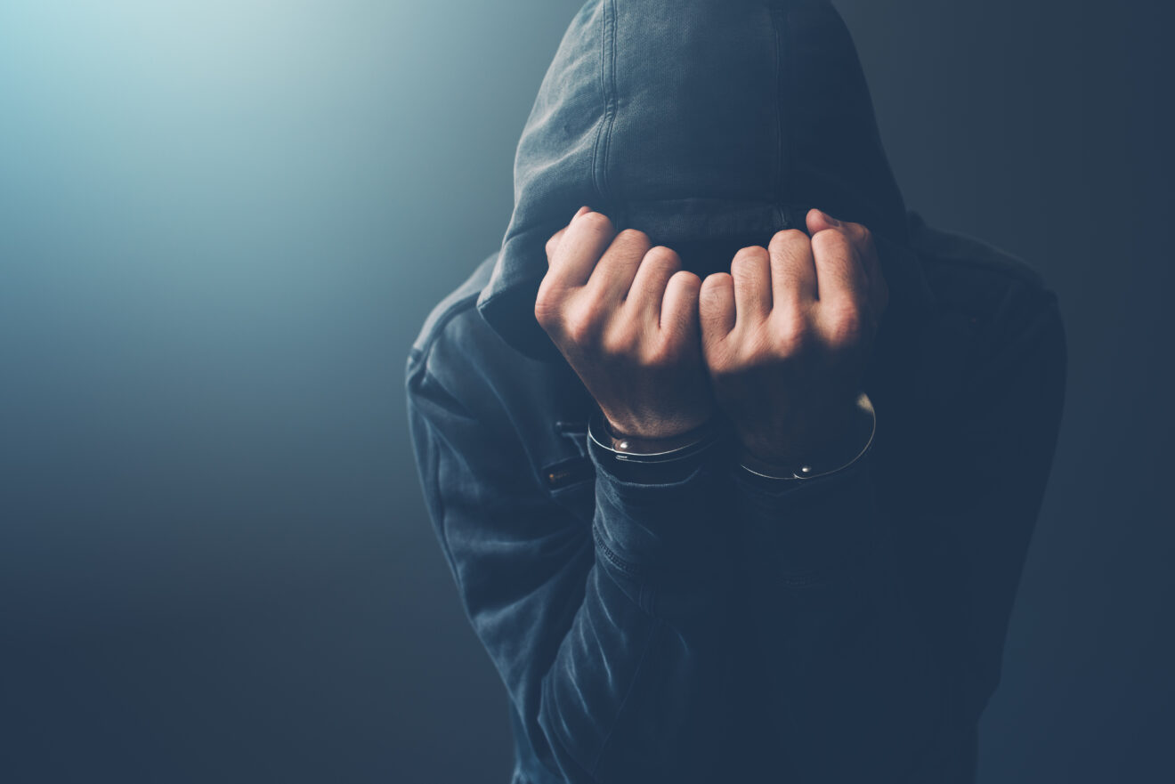 Arrested computer hacker with handcuffs wearing hooded jacket