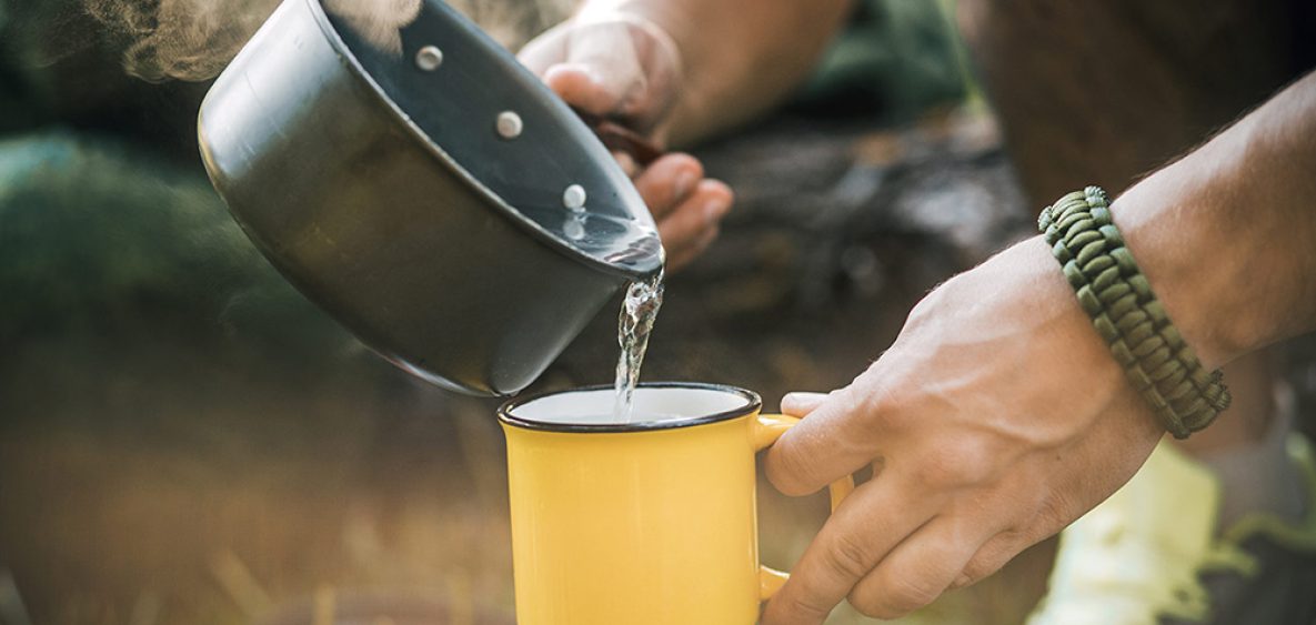 Man traveler hands holding a Cup of tea outdoors. The concept of adventure, travel, tourism and camping. Tourist drinking tea from a mug in the camp.